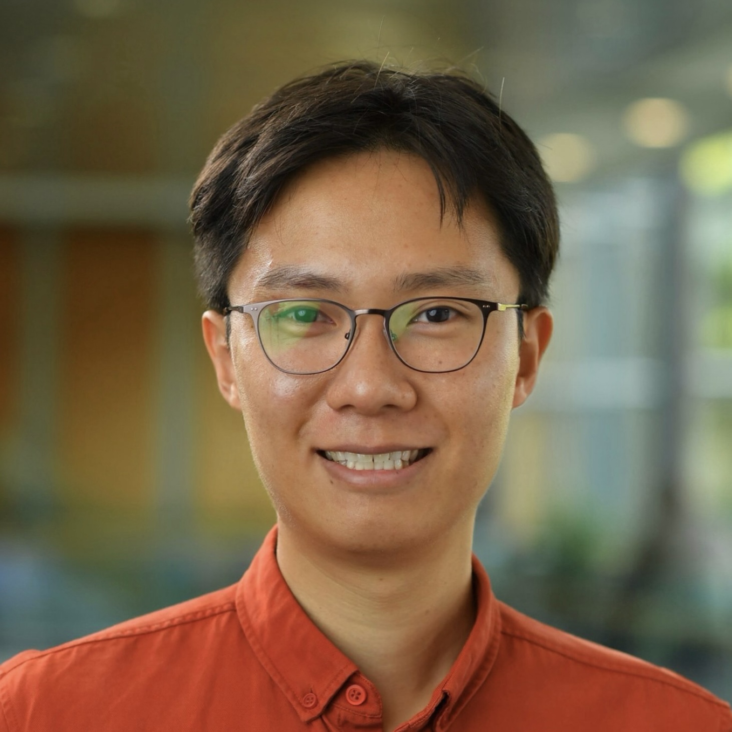 Photograph of a young Asian man with short brown hair, eyeglasses, an orange shirt, and a hint of a smile.